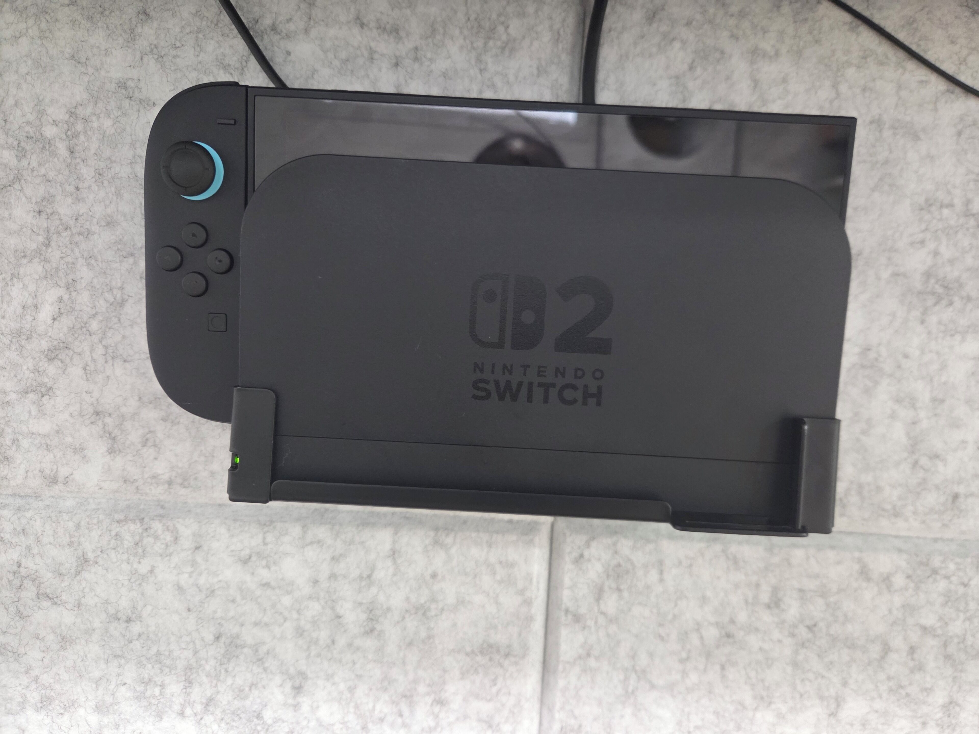 A Nintendo Switch console with a detachable screen, placed on a tiled surface.