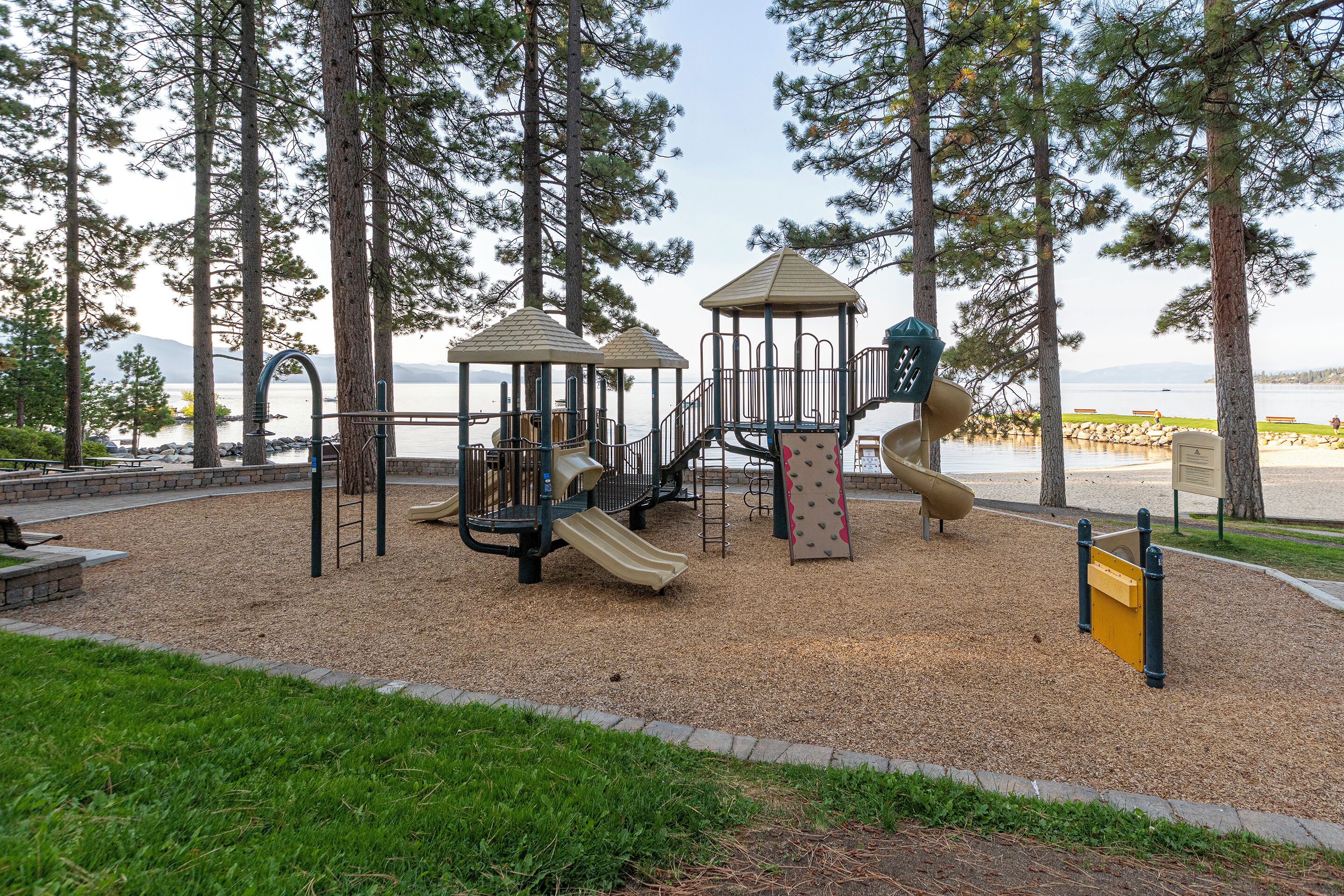 A playground with climbing structures, slides, and a play area surrounded by trees.
