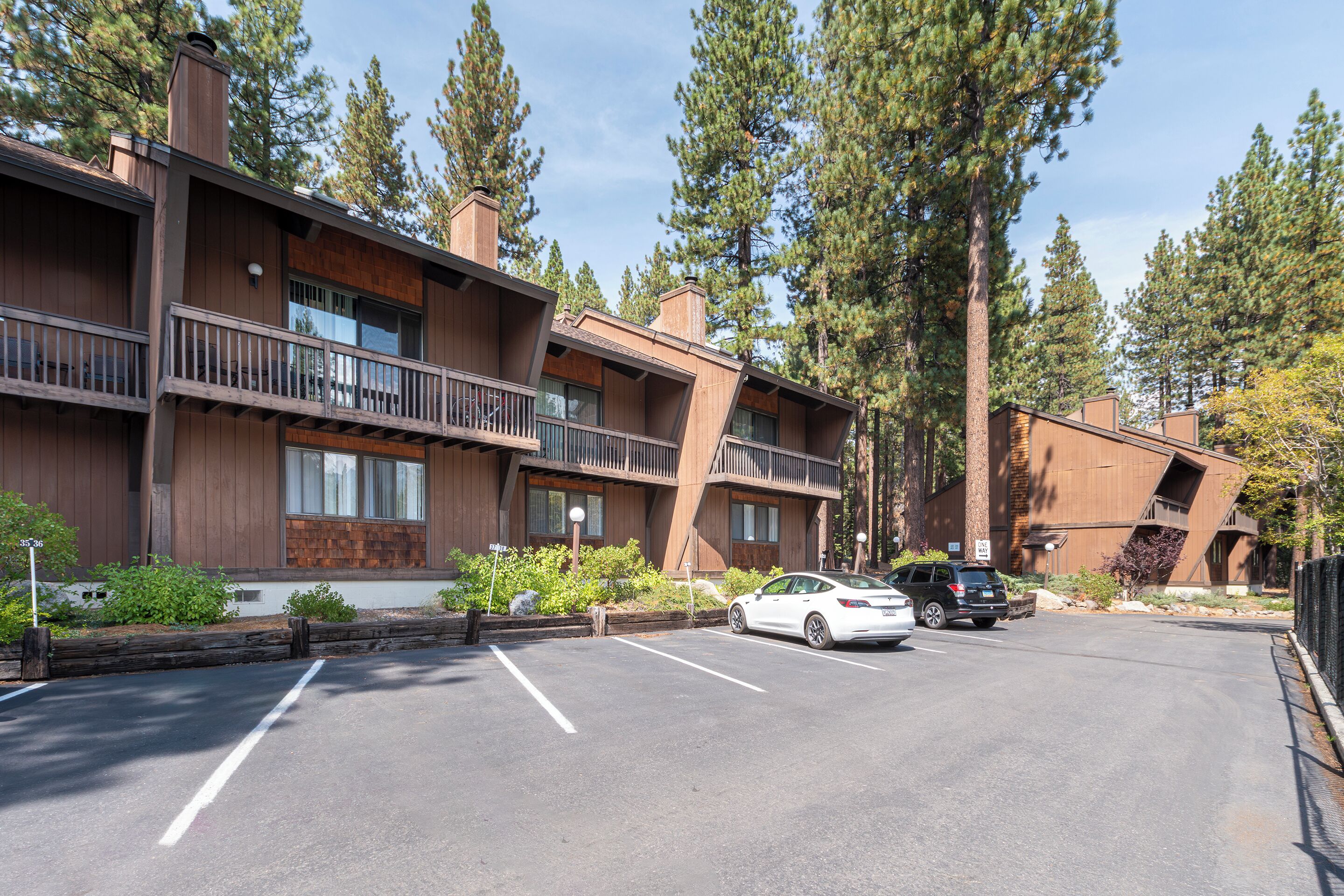 A multi-story building with a parking lot, surrounded by tall trees.