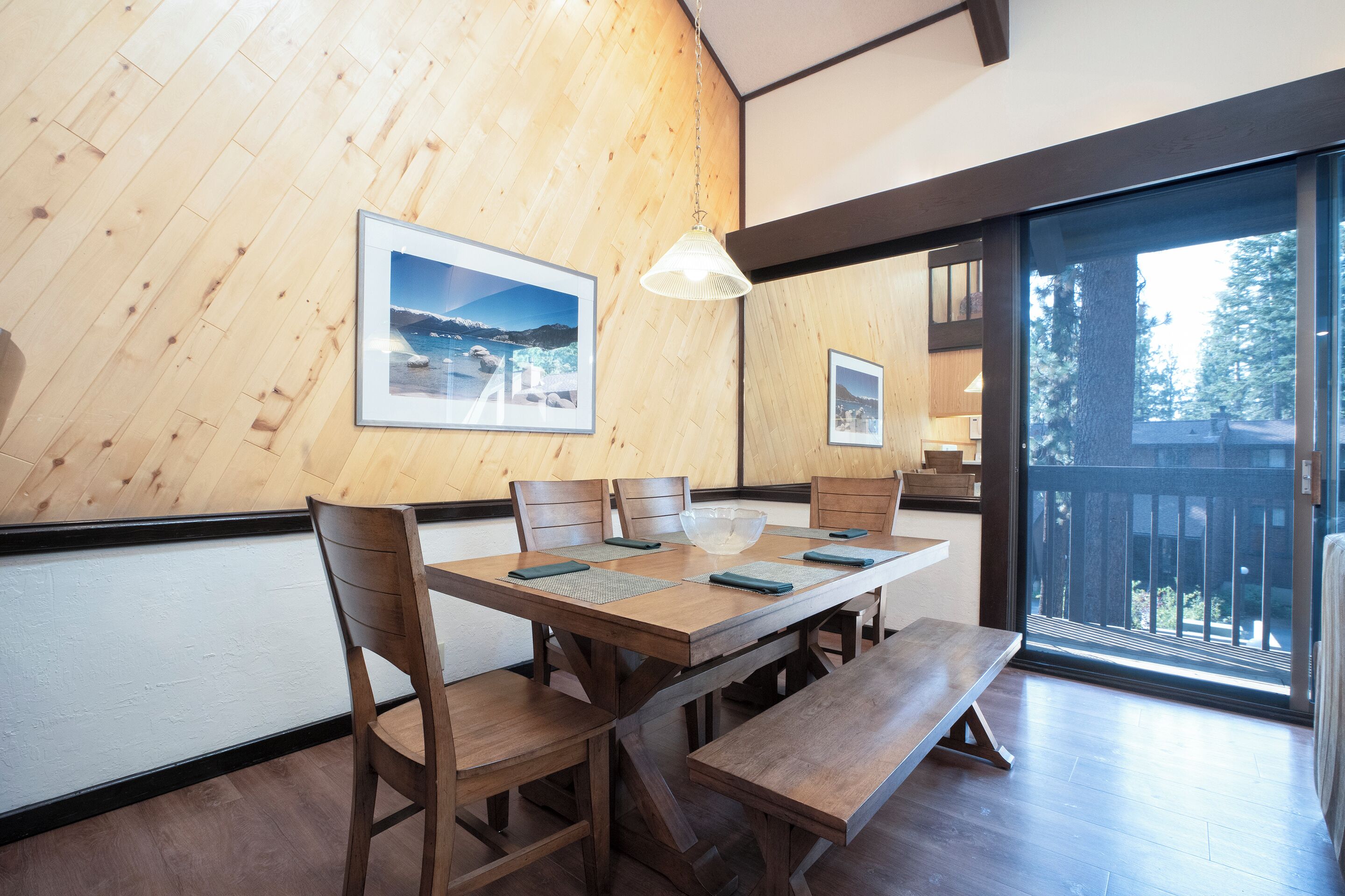 Un comedor de madera con una mesa grande, bancos y sillas. Hay cuadros enmarcados en la pared y una lámpara colgante.