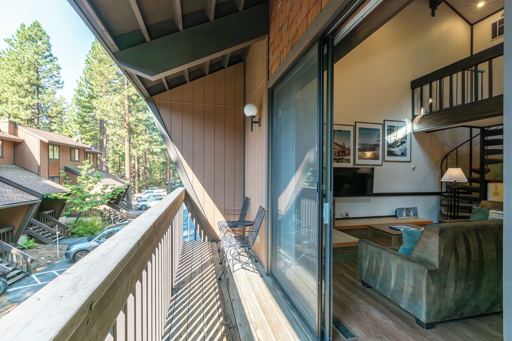Un intérieur moderne avec un balcon donnant sur une zone boisée, un coin salon confortable et un escalier menant à un niveau supérieur.