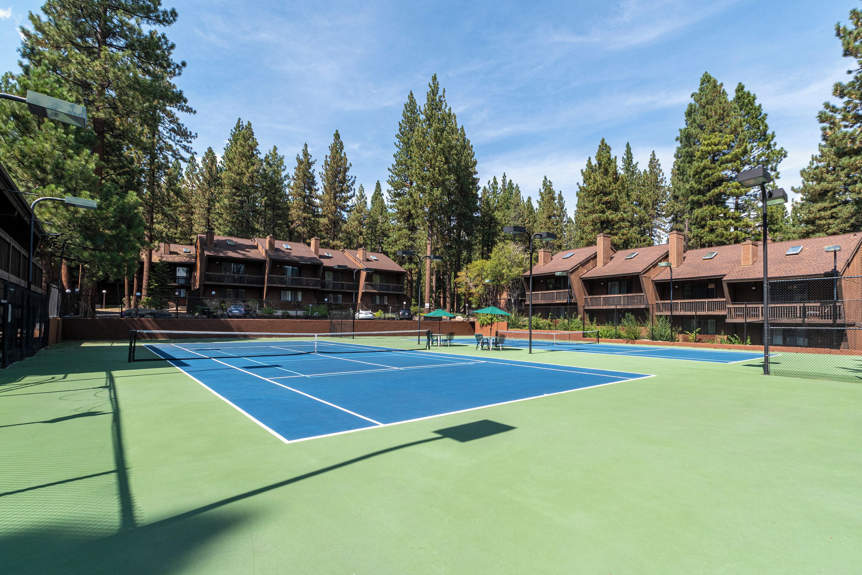 A tennis court with a net, surrounded by buildings with balconies and trees.
