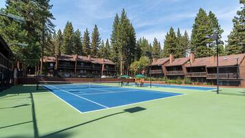 A tennis court with a net, surrounded by buildings with balconies and trees.