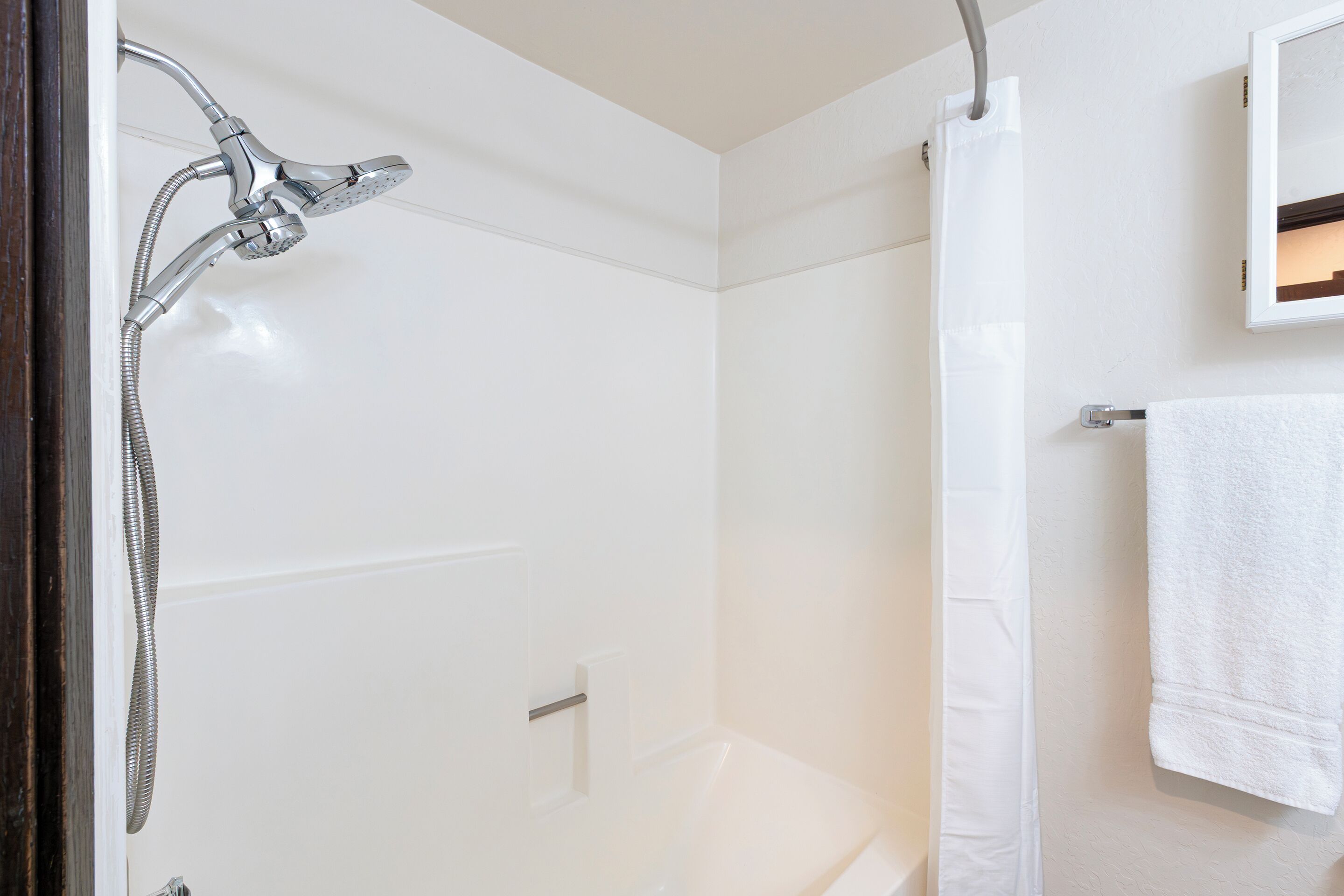 A bathroom with a shower, a white bathtub, and a towel hanging on a rack.