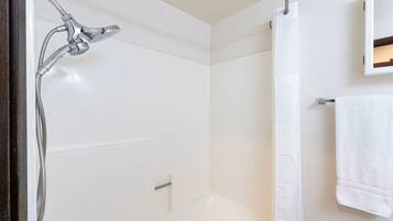Une salle de bain avec une douche, une baignoire blanche et une serviette suspendue à un porte-serviettes.