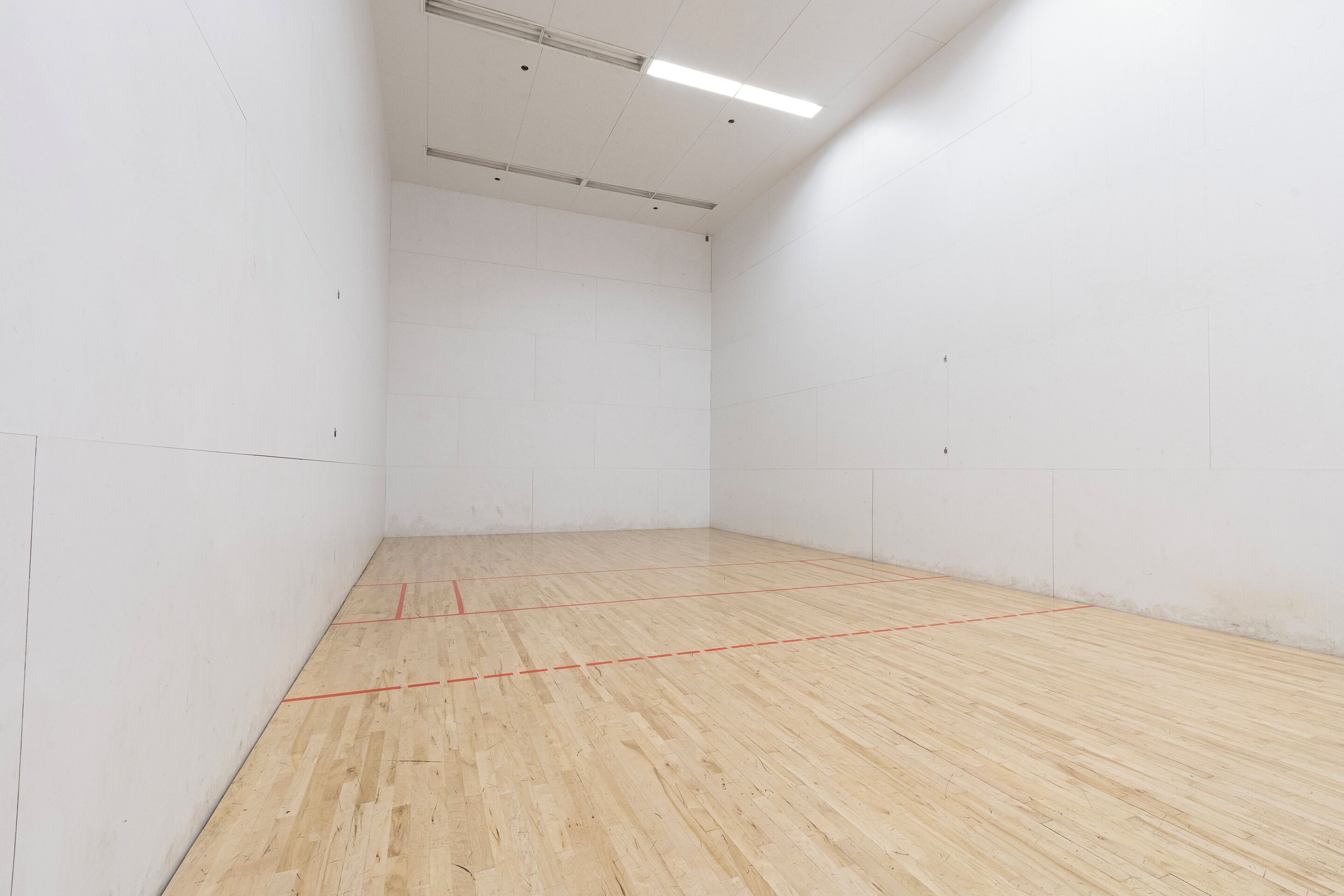 En rummelig squashbane indendørs med trægulv og hvide vægge.