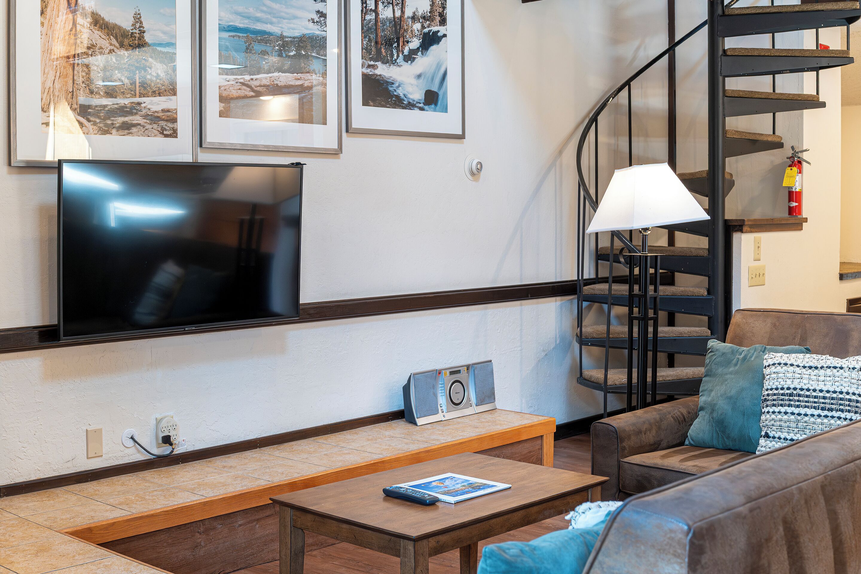 A living room with a flat-screen TV, a sofa, a coffee table, a lamp, and a staircase.