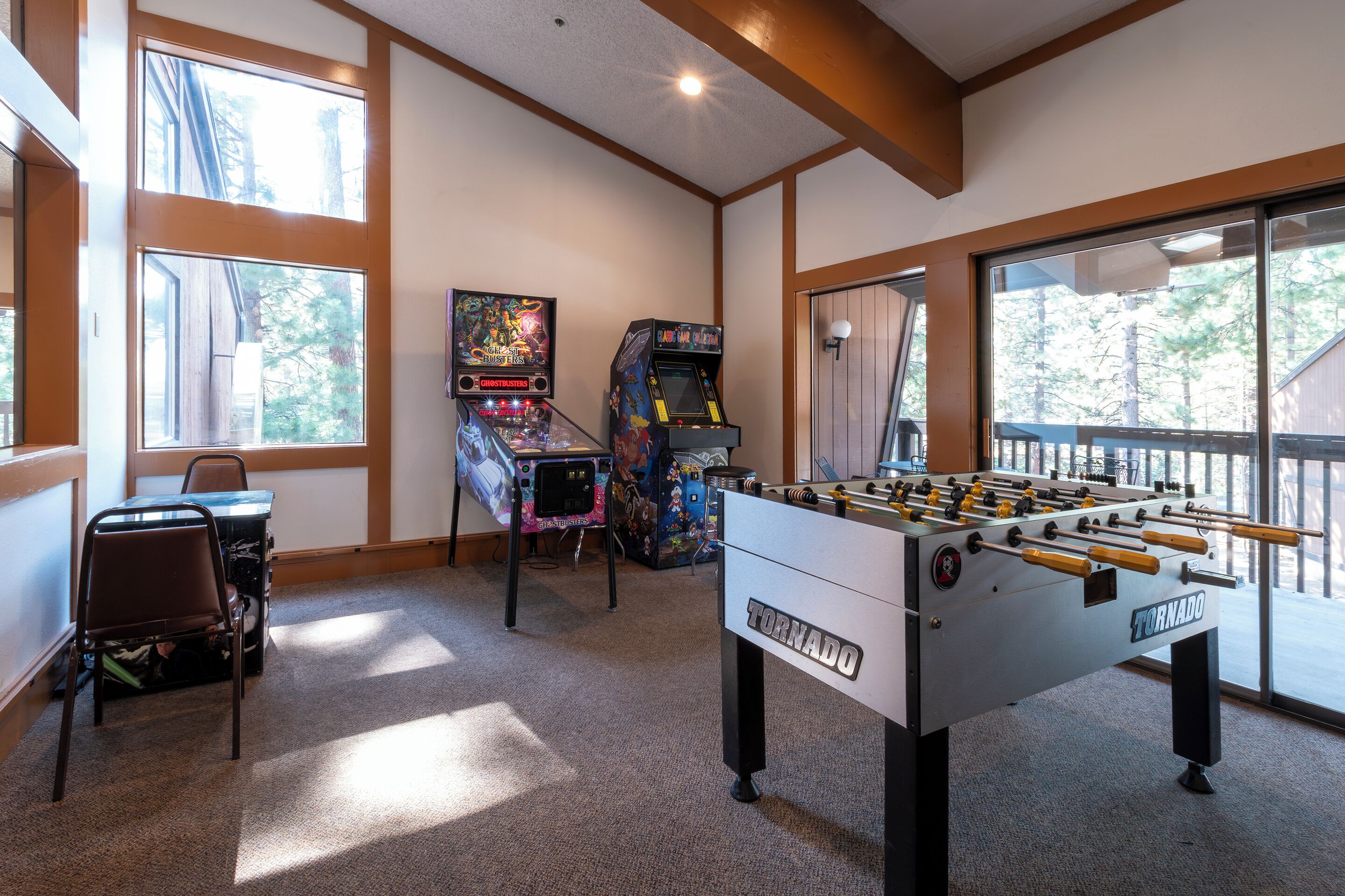 A room with a foosball table labeled "Tornado," two arcade machines, a window with a view of trees, and a chair.