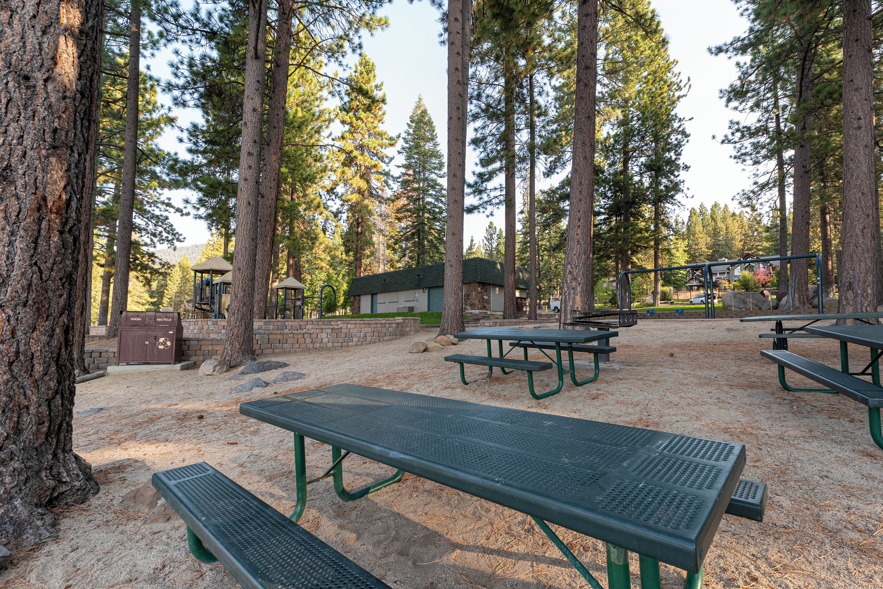 A campground with picnic tables, a recycling bin, and a building in a forested area.