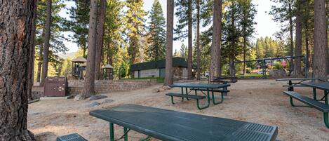A campground with picnic tables, a recycling bin, and a building in a forested area.