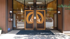 L’entrée d’un hôtel, avec une façade en bois, des portes en verre et un paillasson noir devant l’entrée.