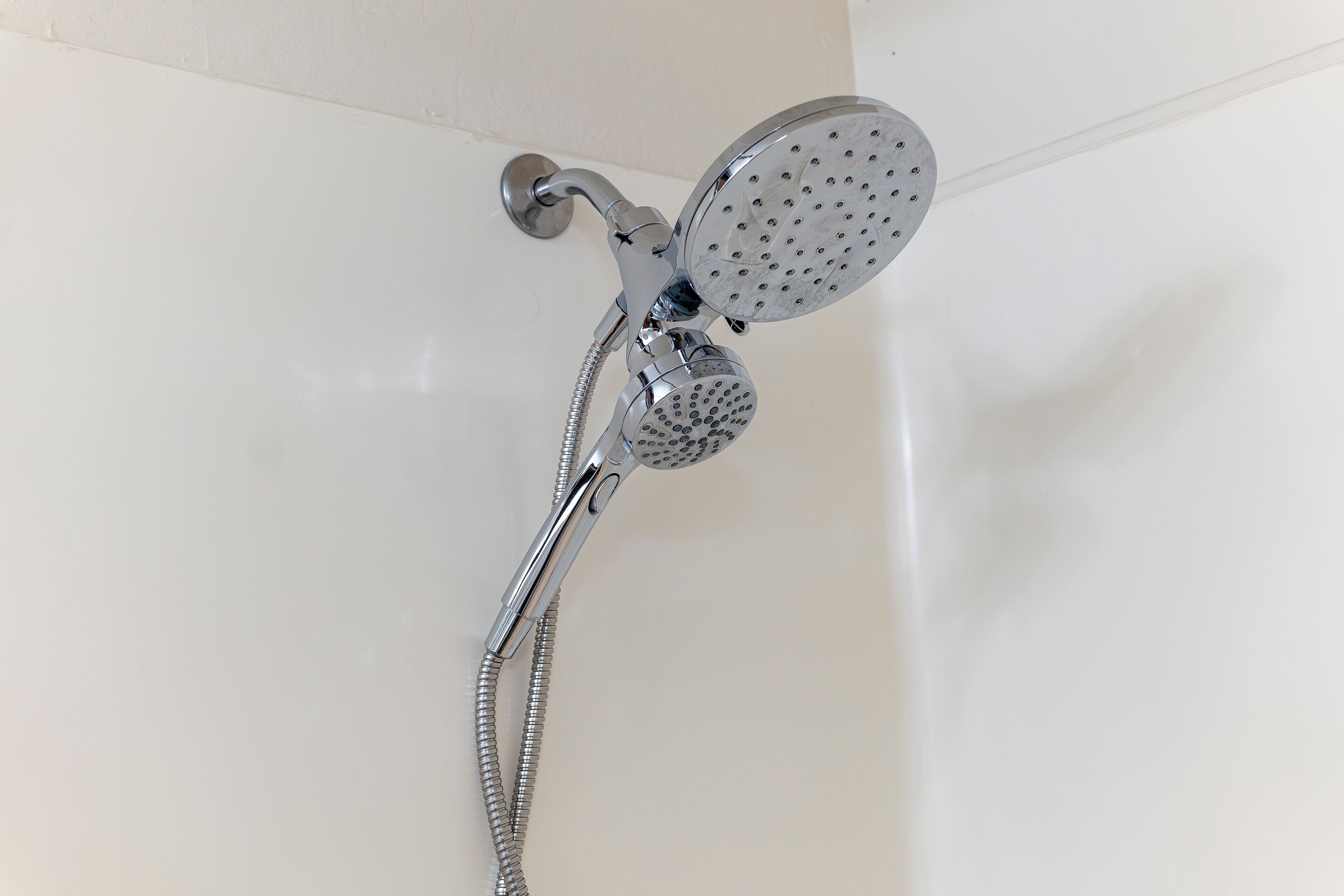 A chrome showerhead with a flexible hose, mounted on a white wall.