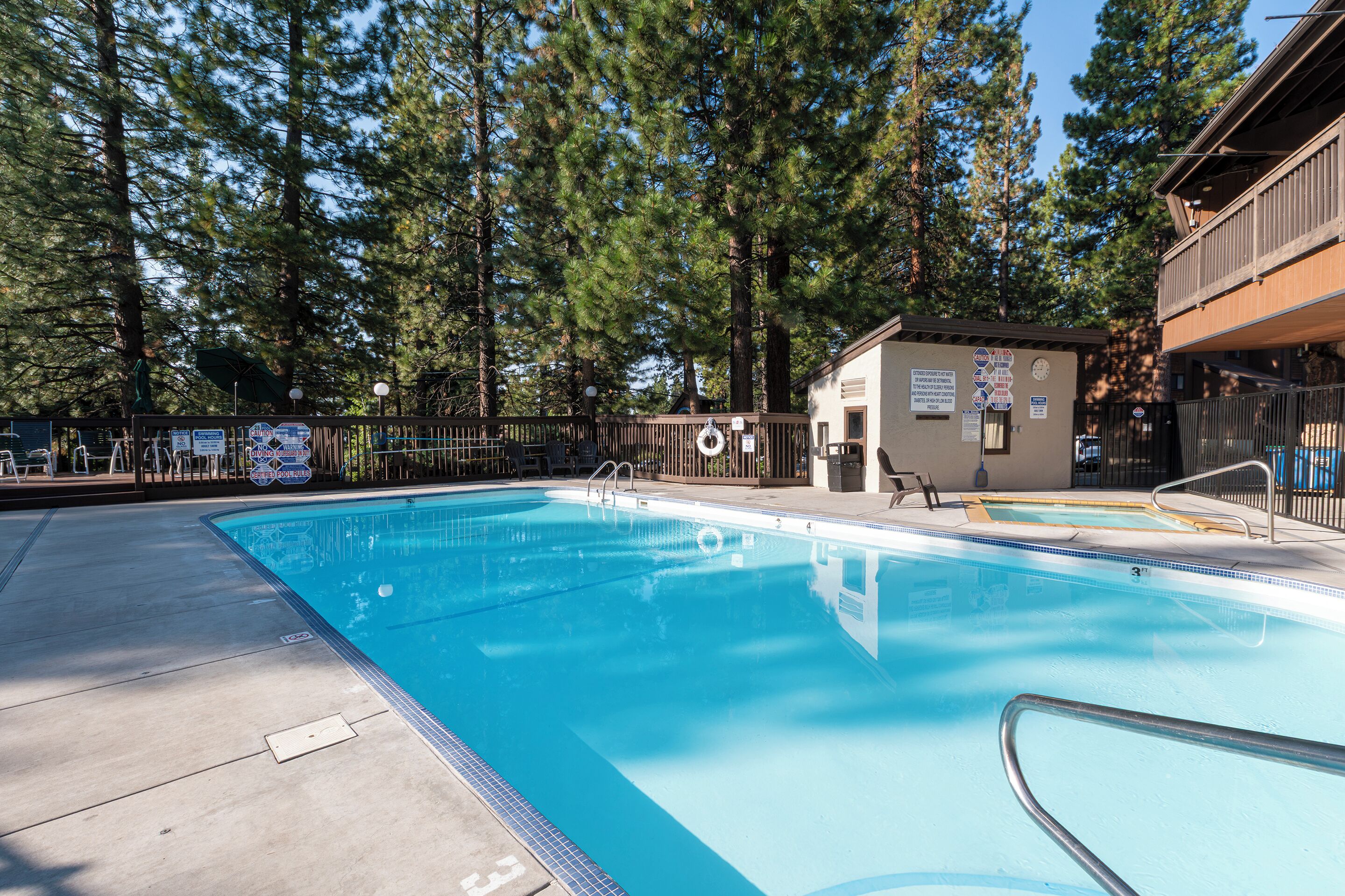 A swimming pool with a wooden deck and a small building in the background.