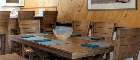 A wooden dining table with a large glass bowl centerpiece, surrounded by wooden chairs with blue placemats.