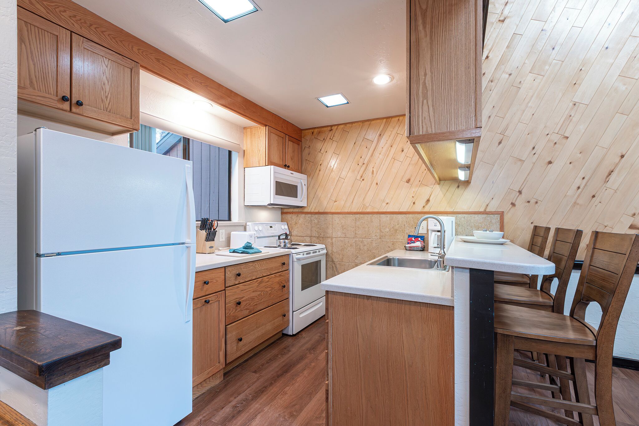 Une cuisine avec des meubles de rangement en bois, un réfrigérateur blanc, un four à micro-ondes, une cuisinière et un évier.