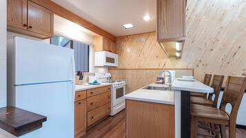 Une cuisine avec des meubles de rangement en bois, un réfrigérateur blanc, un four à micro-ondes, une cuisinière et un évier.