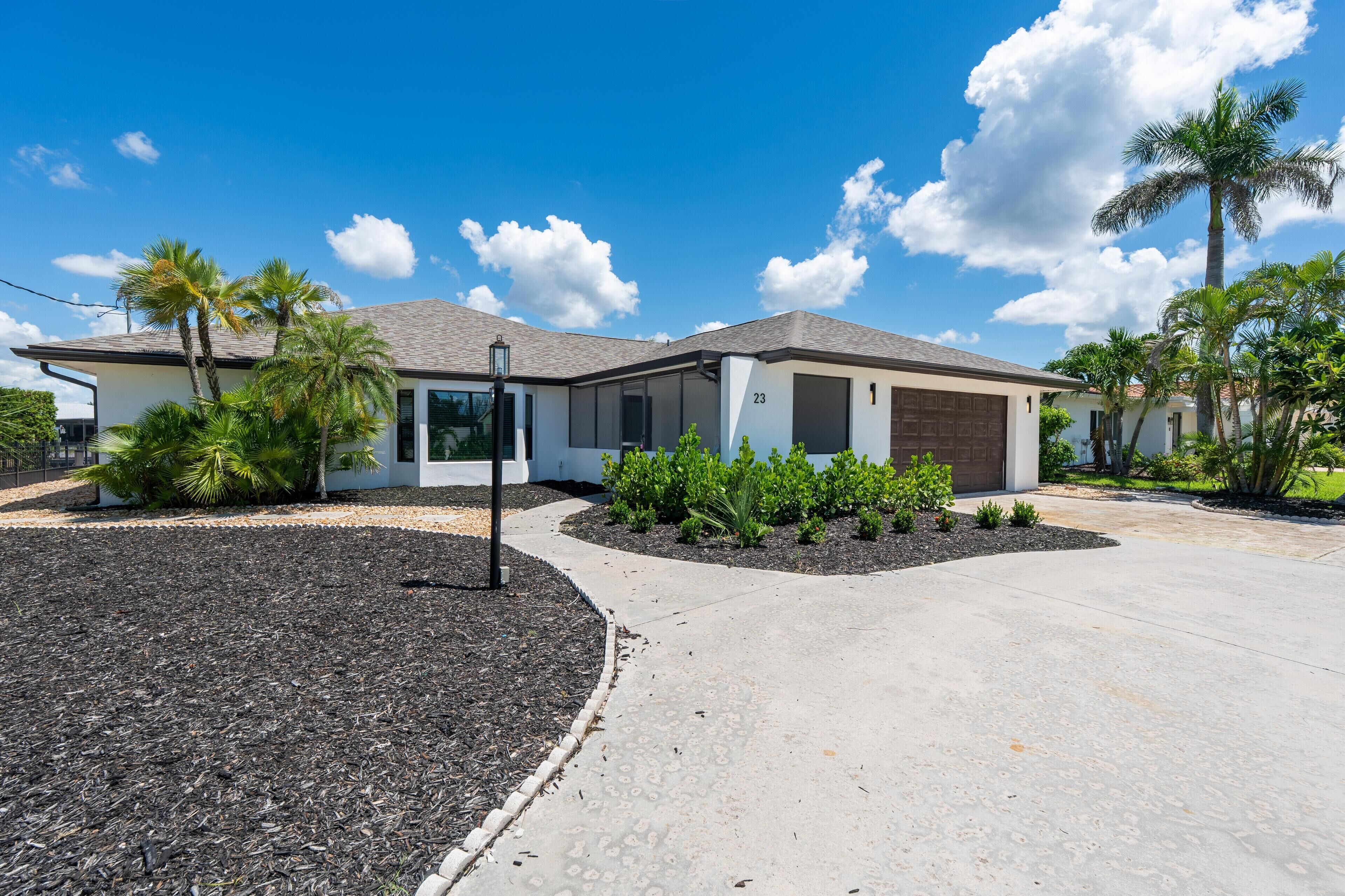 A modern house with a garage, a driveway, and landscaped garden with palm trees.