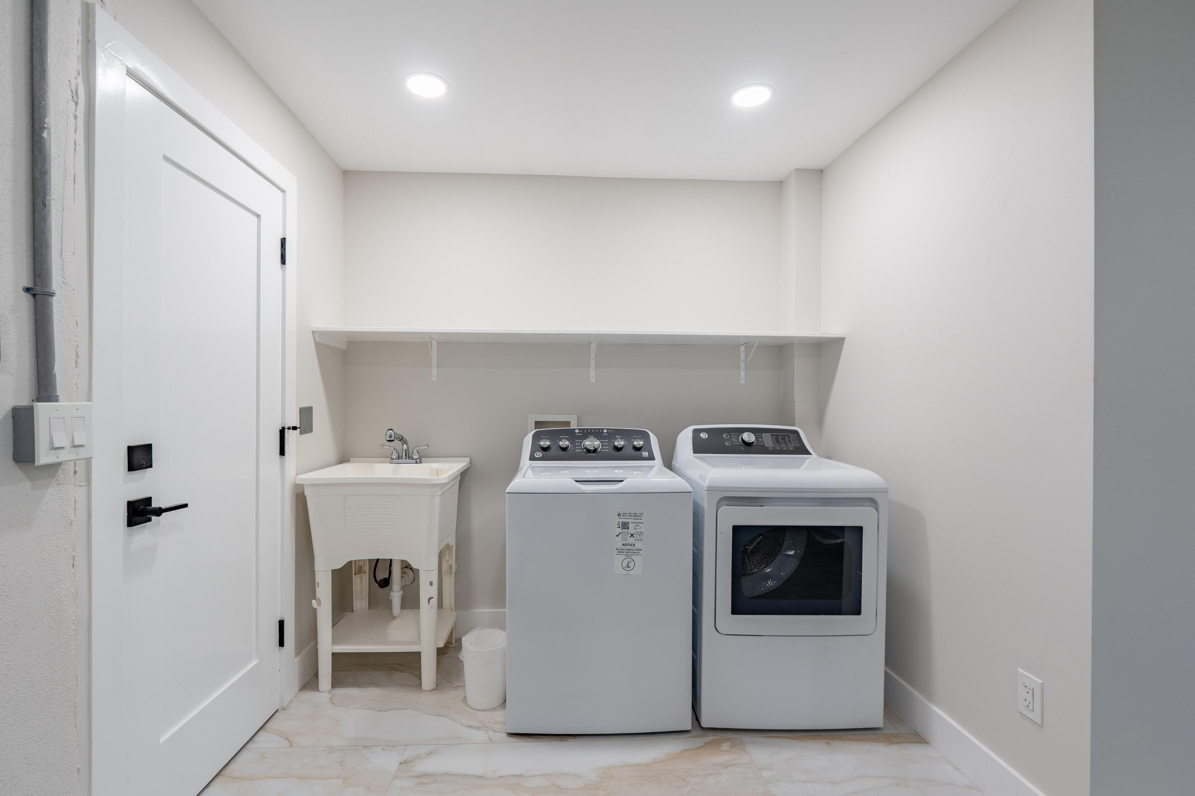 A laundry room with a white door, a washing machine, a dryer, and a small sink.