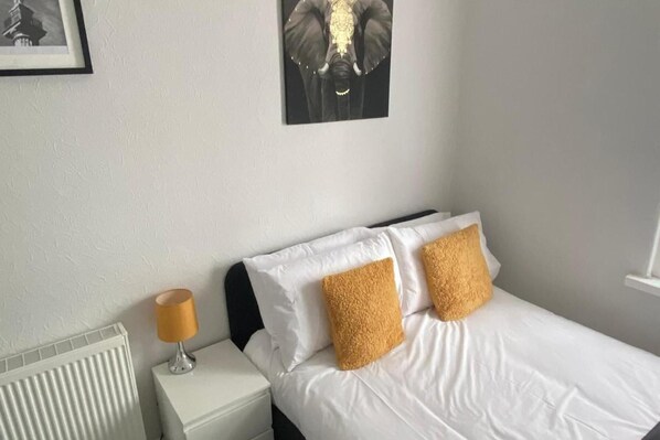 Habitación de hotel con una cama, dos almohadas, una mesita de noche con una lámpara y un cuadro en la pared.