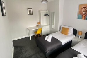 Habitación de hotel con dos camas, un escritorio, una silla, un aparador y un espejo.
