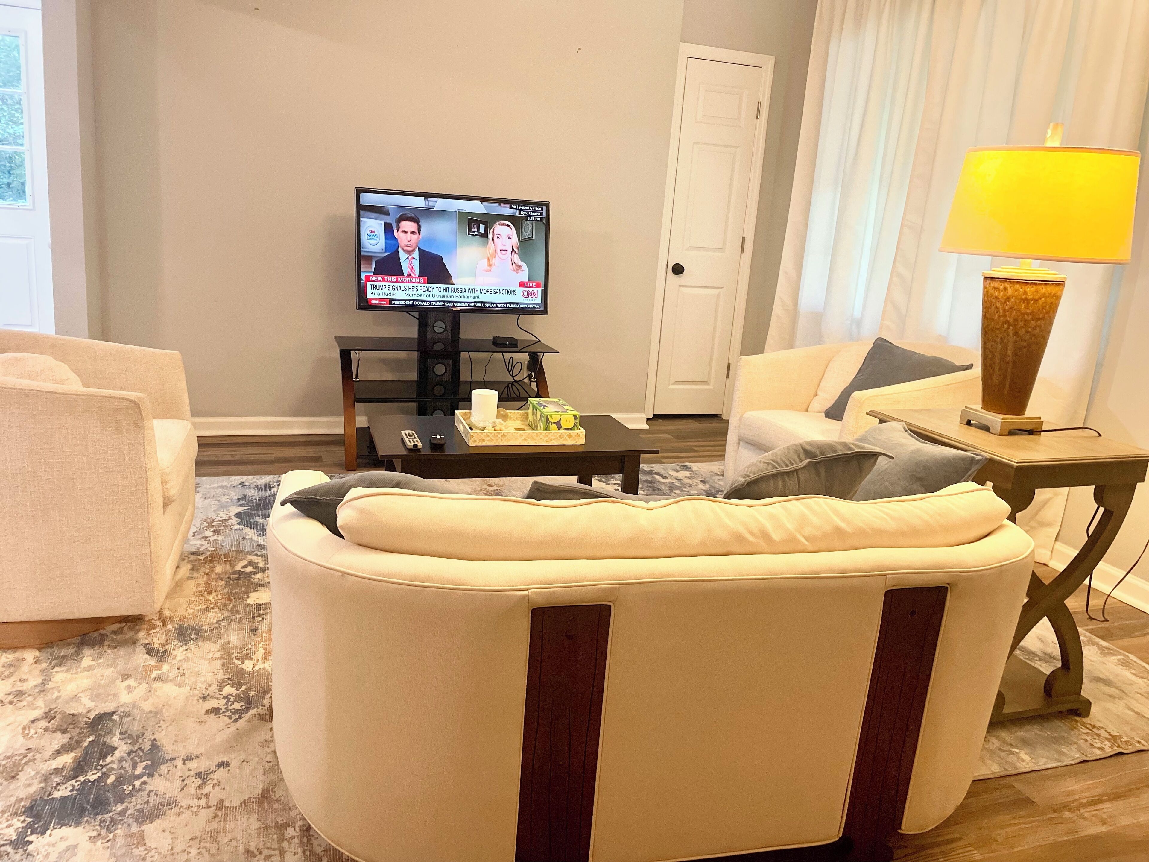 A living room with a sofa, a coffee table with remote control, a lamp, and a television displaying a news program.