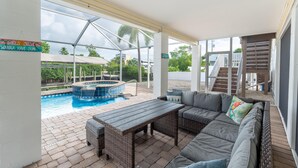 A covered outdoor area with a pool, a wooden table, and a sofa. - Beach Bound (Fort Myers Beach)