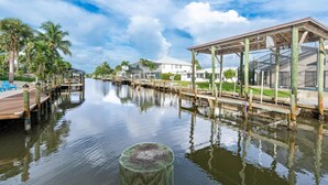 A waterfront property with a dock, wooden pier, and a covered area with a glass enclosure. - Beach Bound (Fort Myers Beach)