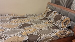 A bed with a patterned bedspread and pillows, a wooden headboard, and a wall with vertical lines. - Sea view villa (Shrivardhan)