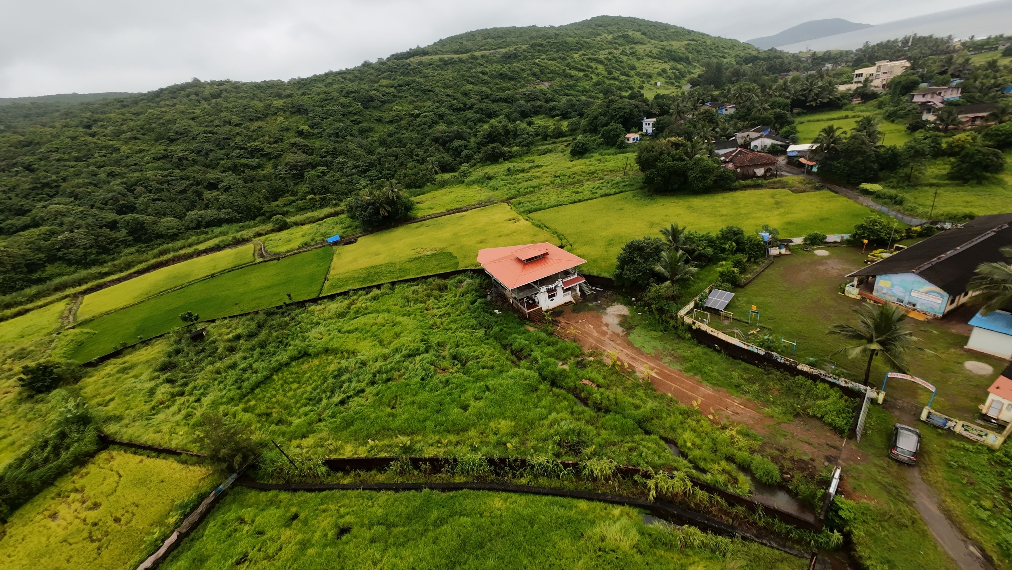 A rural landscape with terraced fields, a small house with a red roof, and scattered buildings.