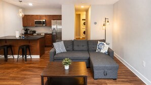 A modern kitchen with stainless steel appliances, a grey sectional sofa, and a wooden coffee table. - Cozy Luxe Suite R&R HoF, Casino, Stadium, Airport (Cleveland)