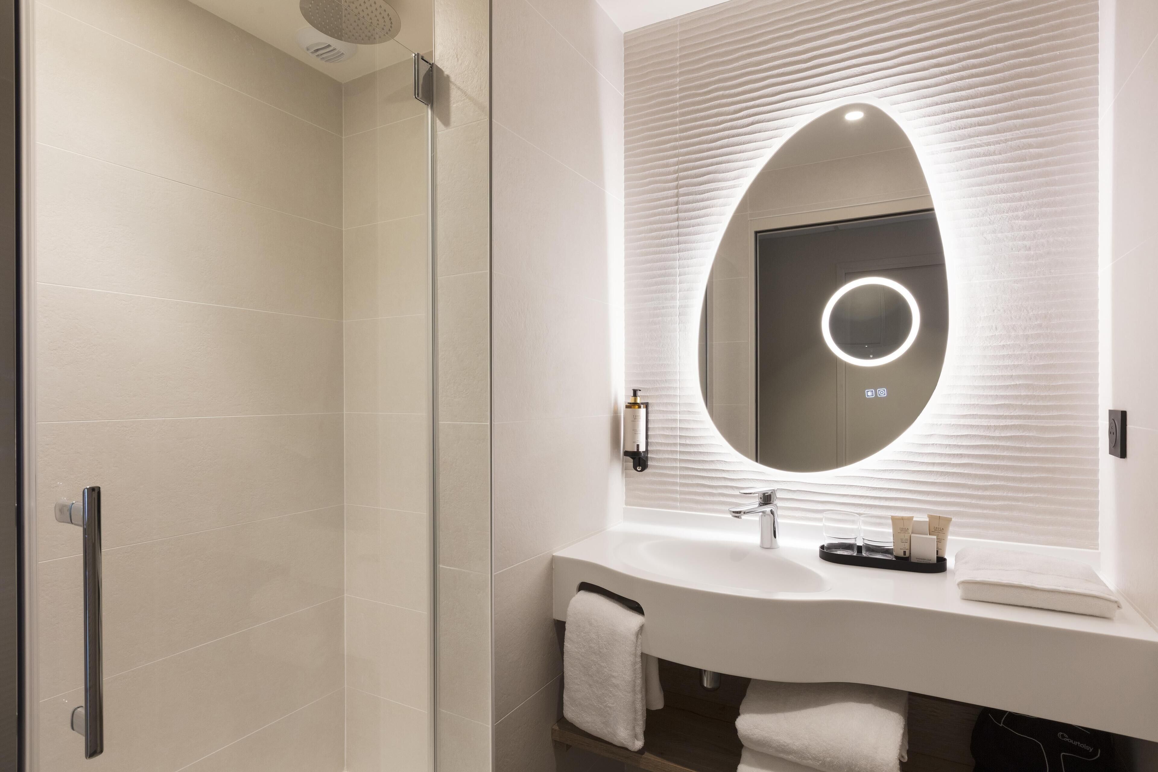 Une salle de bain moderne avec une douche à parois de verre, un meuble-lavabo blanc doté d’un miroir rond et un porte-serviettes.