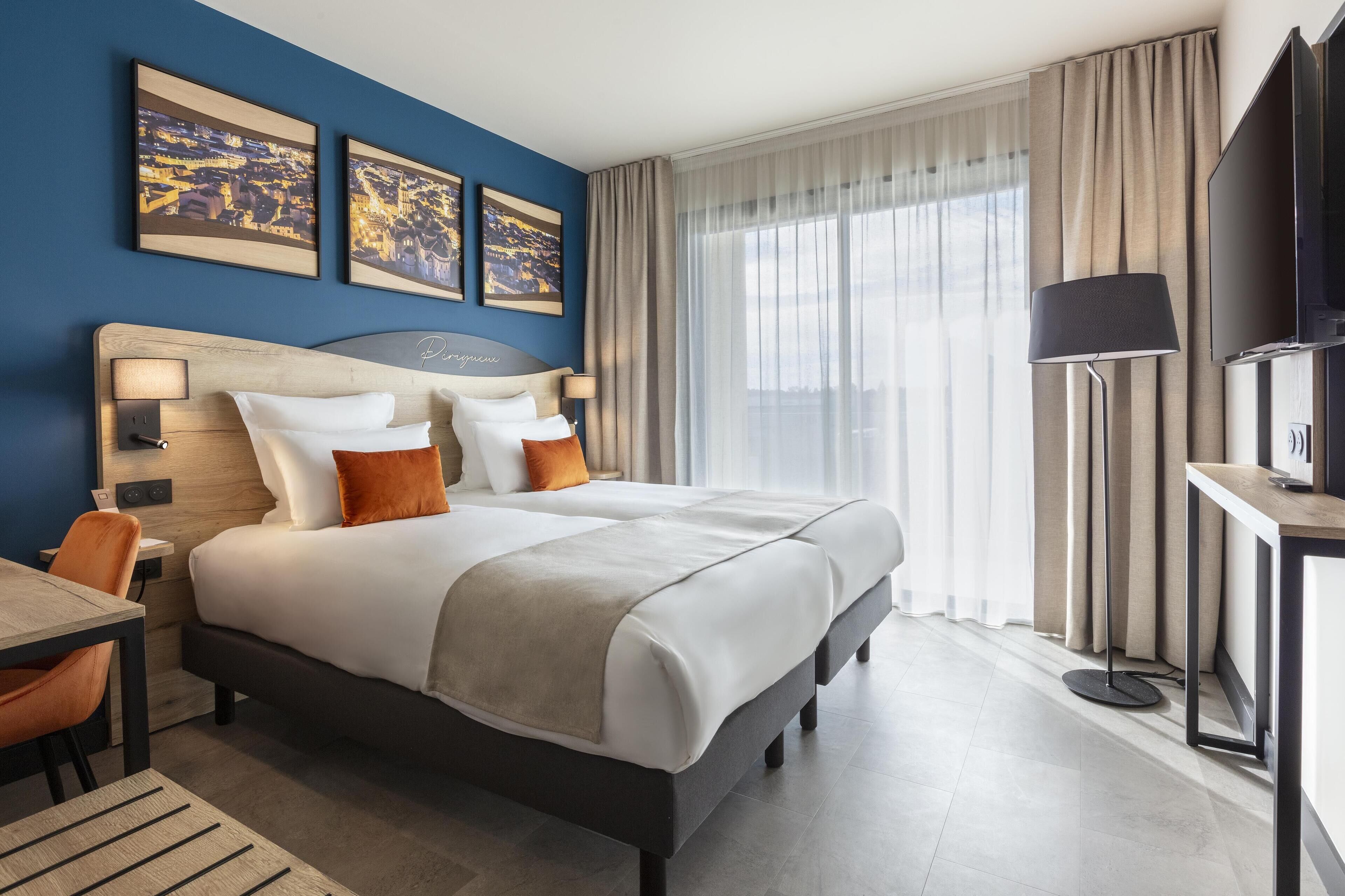 A hotel room with a large bed, a desk, a chair, a TV, and two framed pictures on the wall.