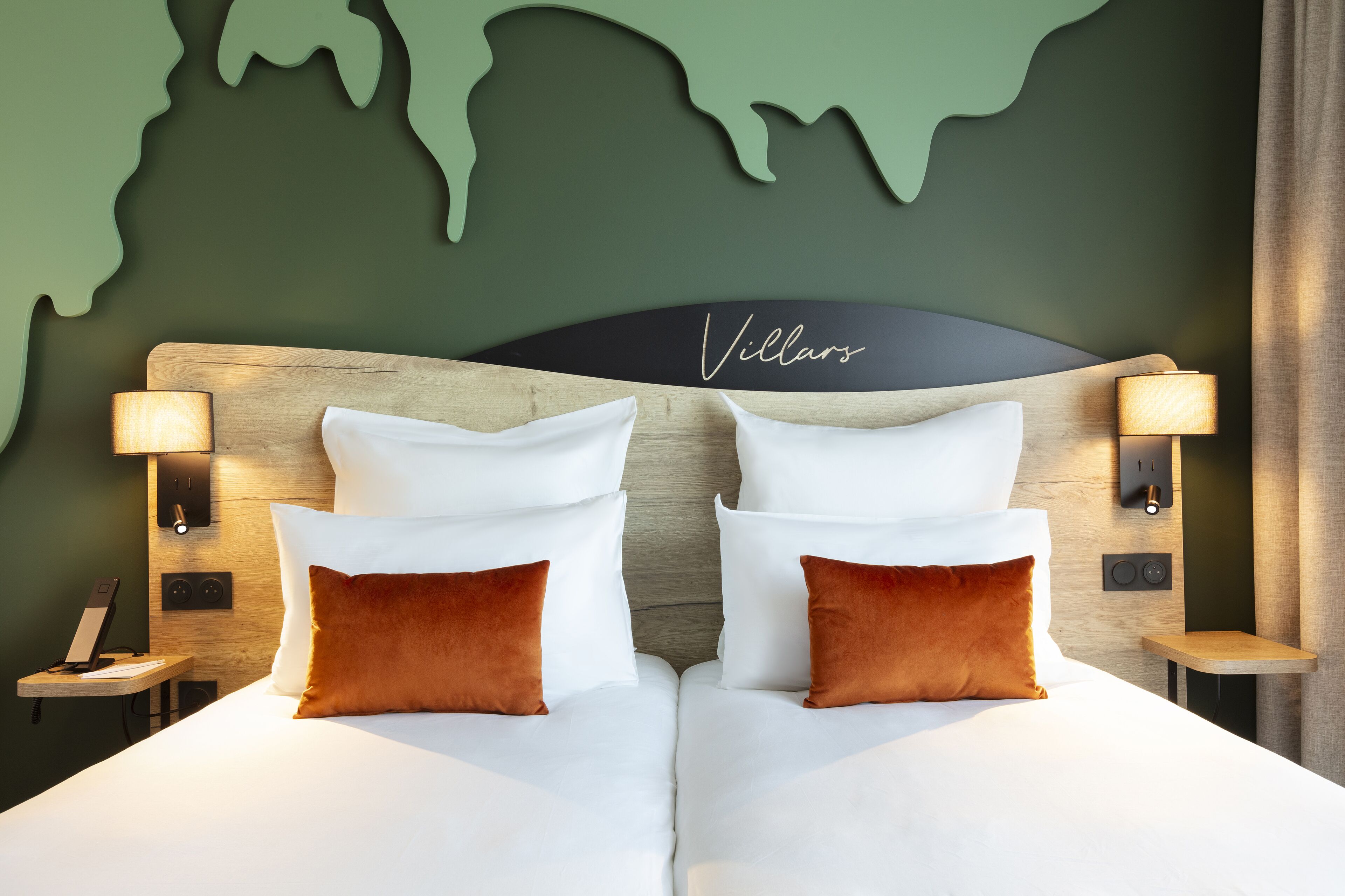 A double bed with white and brown pillows, a wooden headboard, and a world map mural on the wall.