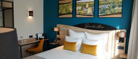 A hotel room with a bed, a desk, a chair, and three framed pictures on the wall.