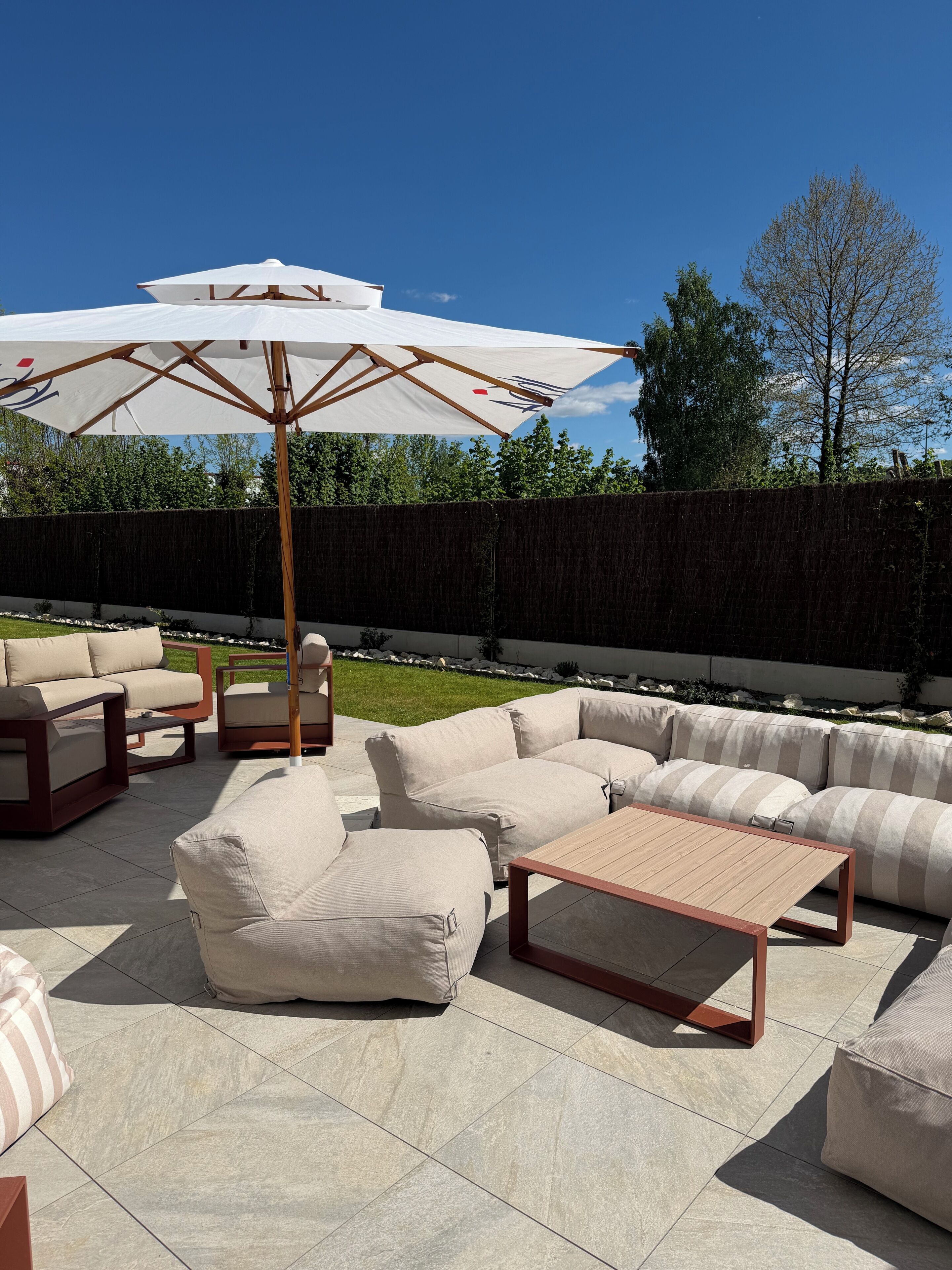 Eine Terrasse im Freien mit beigen Sofas, einem Holztisch und einem großen Sonnenschirm.