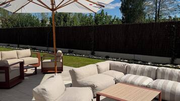 Eine Terrasse im Freien mit beigen Sofas, einem Holztisch und einem großen Sonnenschirm.