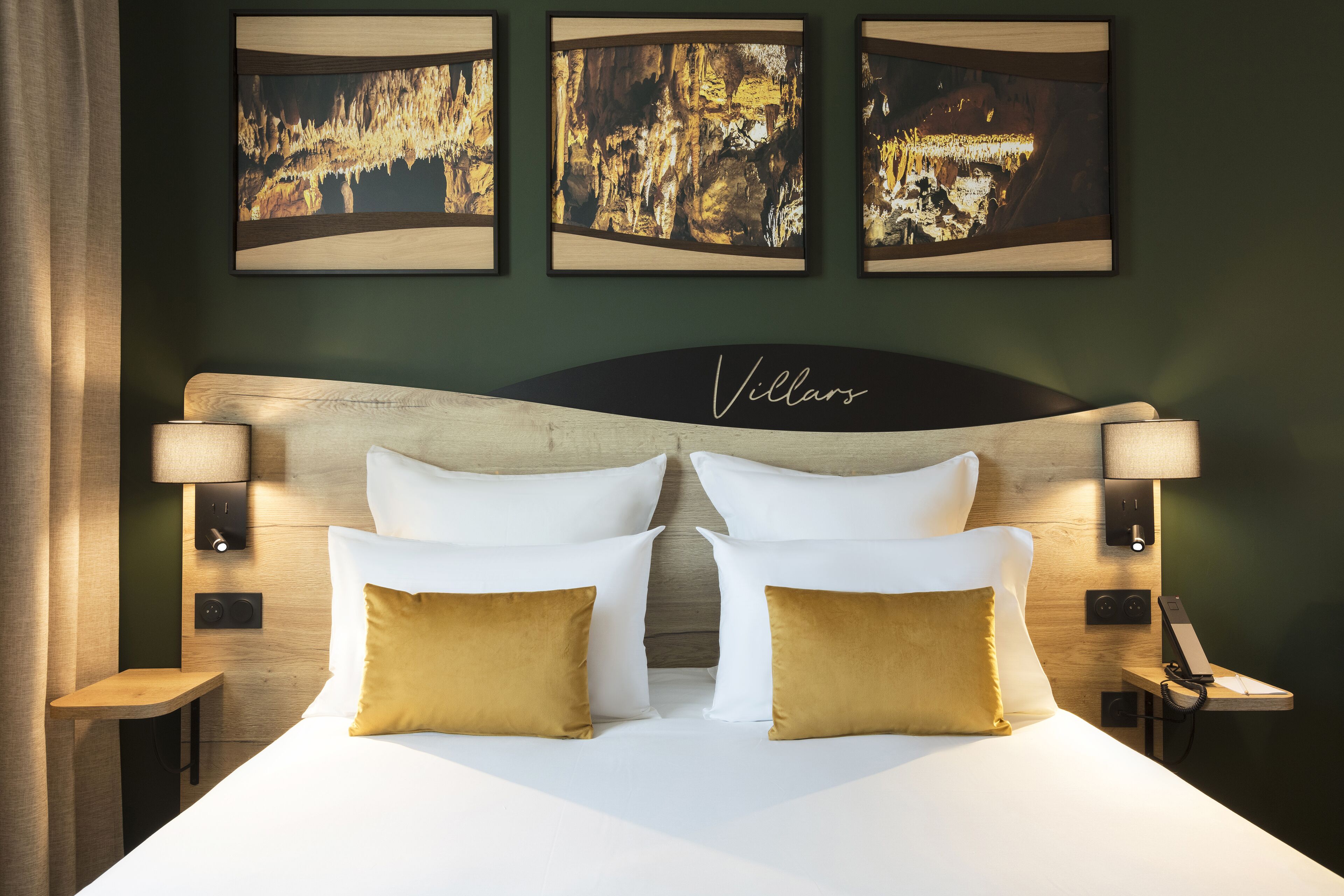 Una habitación de hotel con una cama grande, dos lámparas de noche, una mesita de noche y tres cuadros en la pared.
