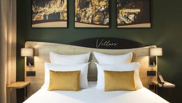 Una habitación de hotel con una cama grande, dos lámparas de noche, una mesita de noche y tres cuadros en la pared.