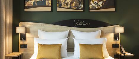 Una habitación de hotel con una cama grande, dos lámparas de noche, una mesita de noche y tres cuadros en la pared.