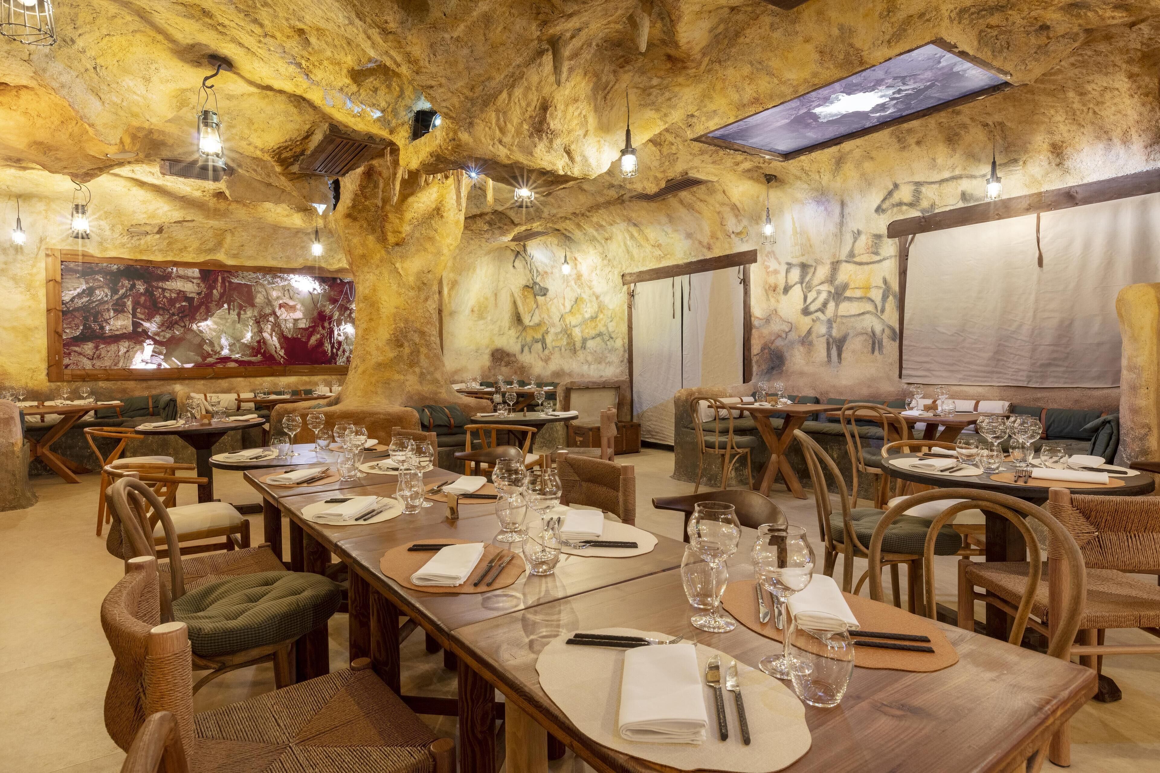Un restaurante con decoración rústica, mesas y sillas de madera, ubicado en un espacio interior que recuerda a una cueva, con paredes y techo de roca natural.