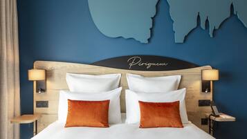 A hotel room with a bed, two pillows, a nightstand, a lamp, and a wall with a silhouette of a city skyline.