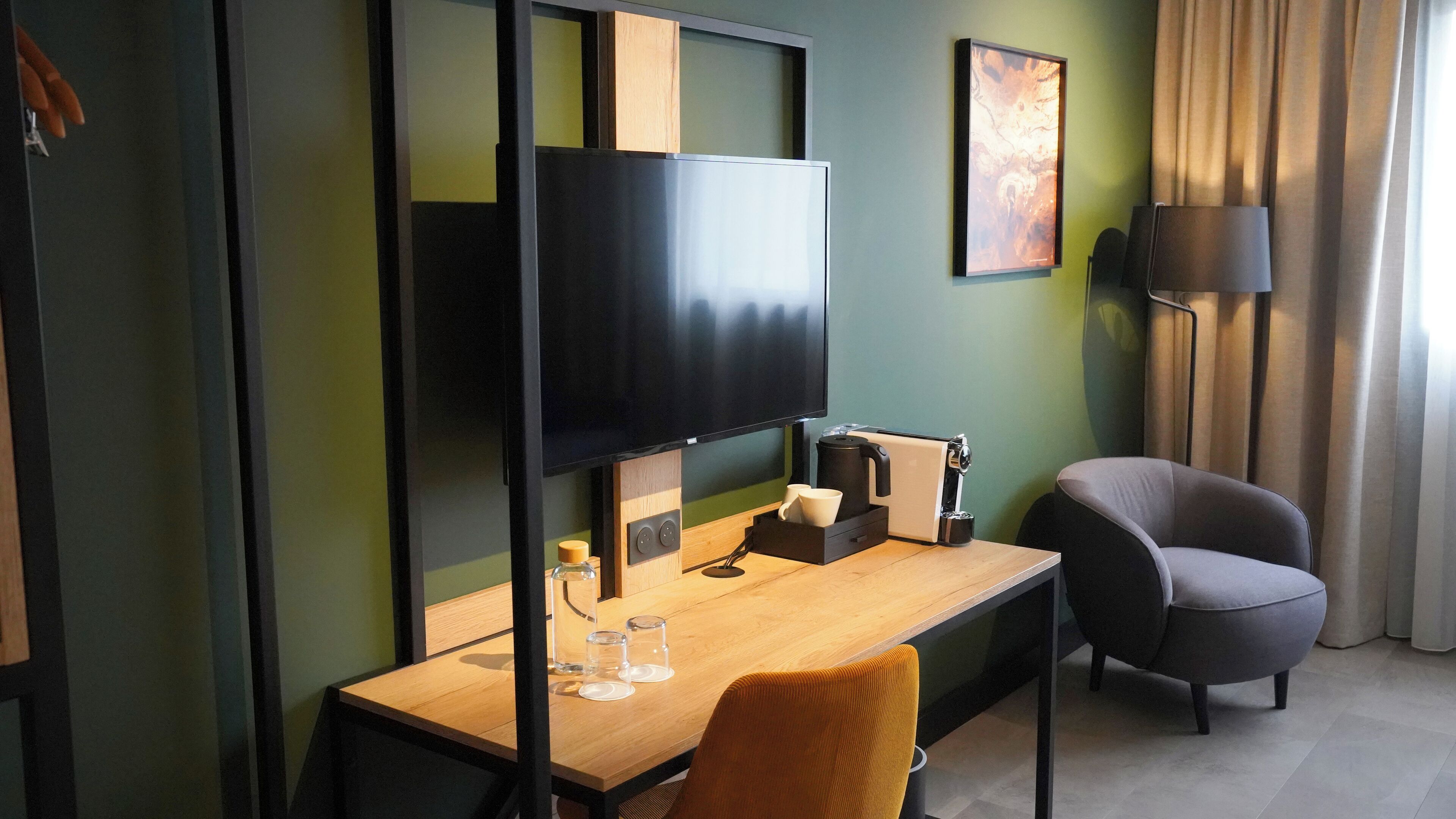 A hotel room with a wooden desk, a flat-screen TV, a coffee maker, and a comfortable armchair.