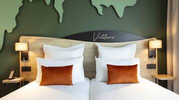 Un lit double avec des oreillers blancs et bruns, une tête de lit en bois, deux lampes de chevet, une décoration murale représentant une carte du monde et un panneau indiquant « Villas ».