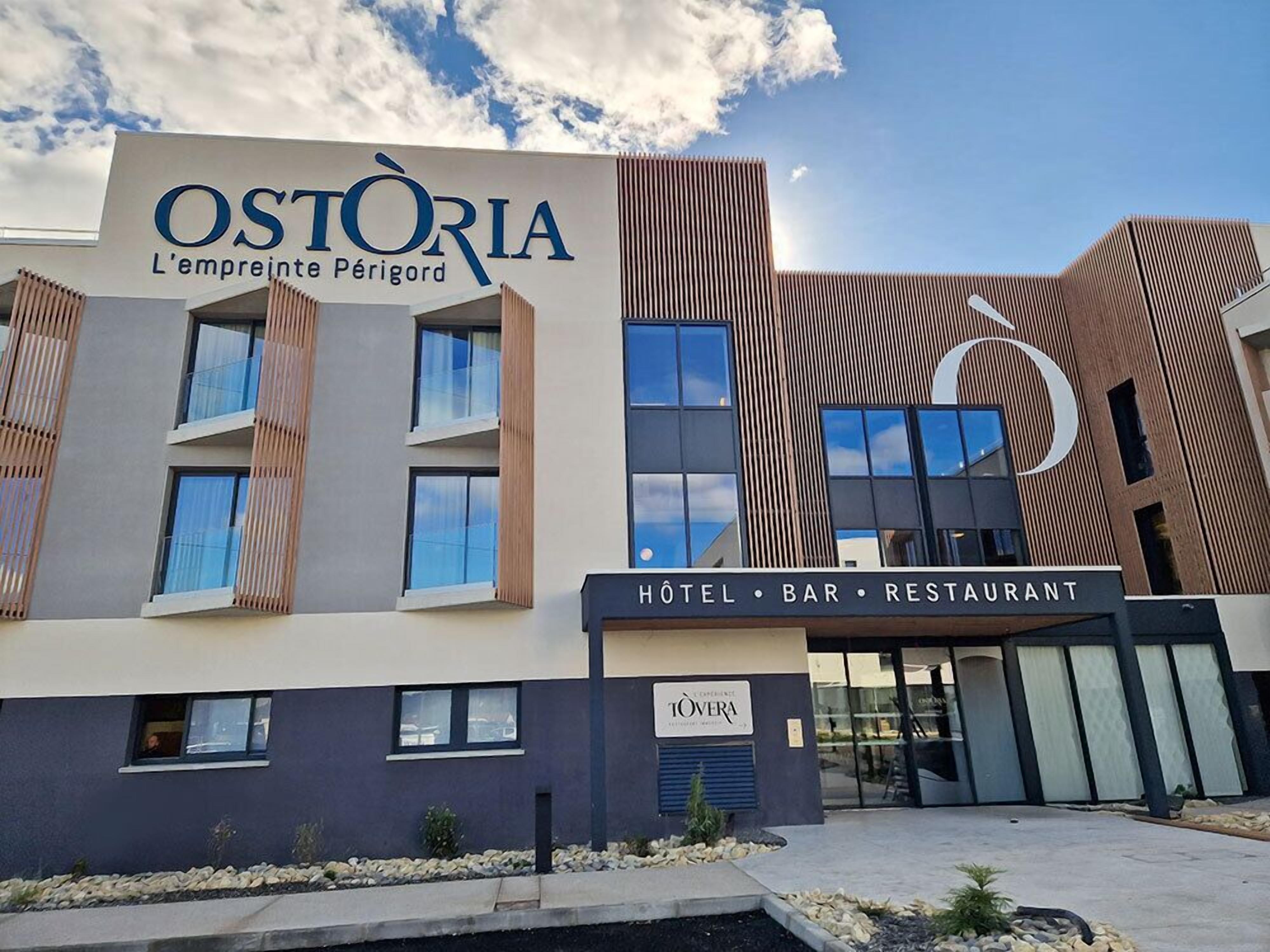 En moderne bygning med et skilt, der angiver 'OSTORIA L'emprente Périgord', og som viser, at det er et hotel, en bar og en restaurant.