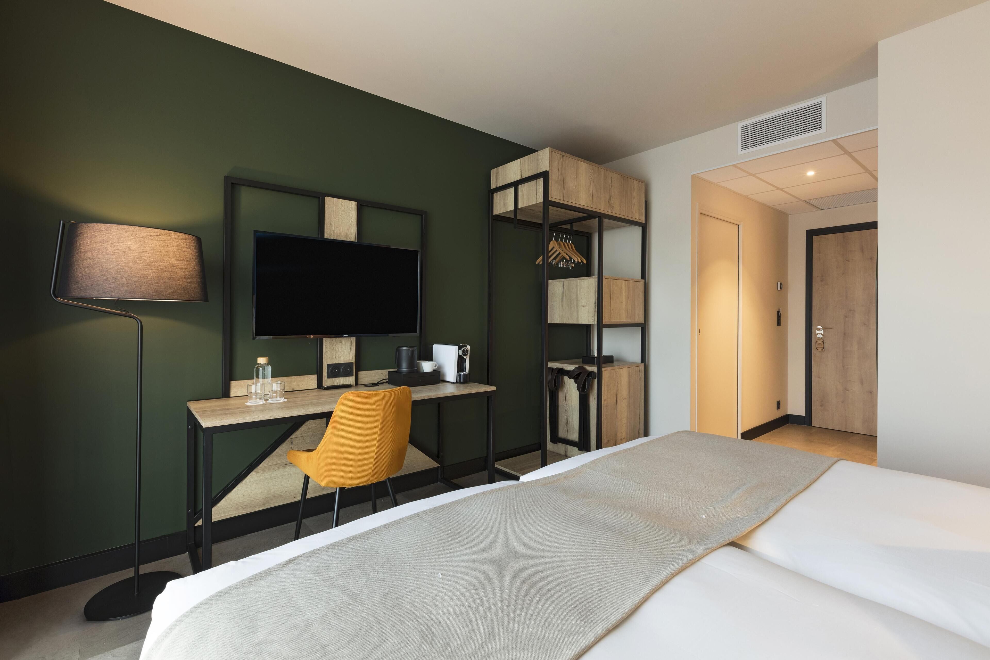 Habitación de hotel con cama, escritorio, silla, televisor y armario.