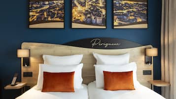 A hotel room with a large bed, two pillows, a headboard with the word "Perigueux," two bedside lamps, and three framed pictures on the wall.