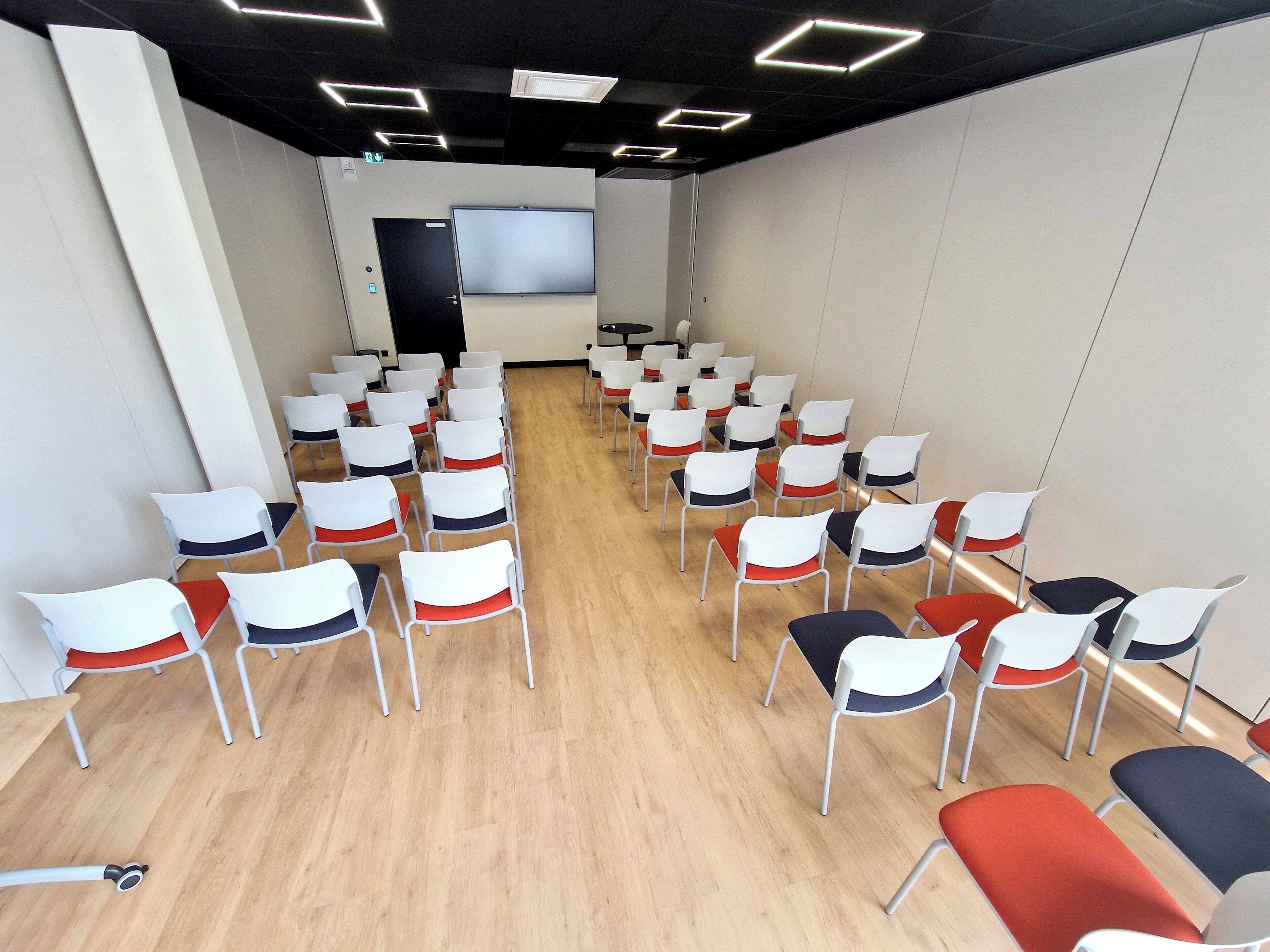 Ein Konferenzraum mit Reihen von Stühlen, einer Projektionsleinwand und einem Holzboden.