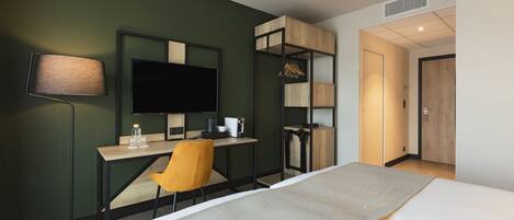 A hotel room with a bed, desk, chair, TV, and wardrobe.