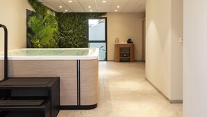 A modern spa area with a large bathtub, a massage table, and a wall with green foliage. - Hôtel Ostoria Périgueux, BW Signature Collection (Marsac-sur-l'Isle)