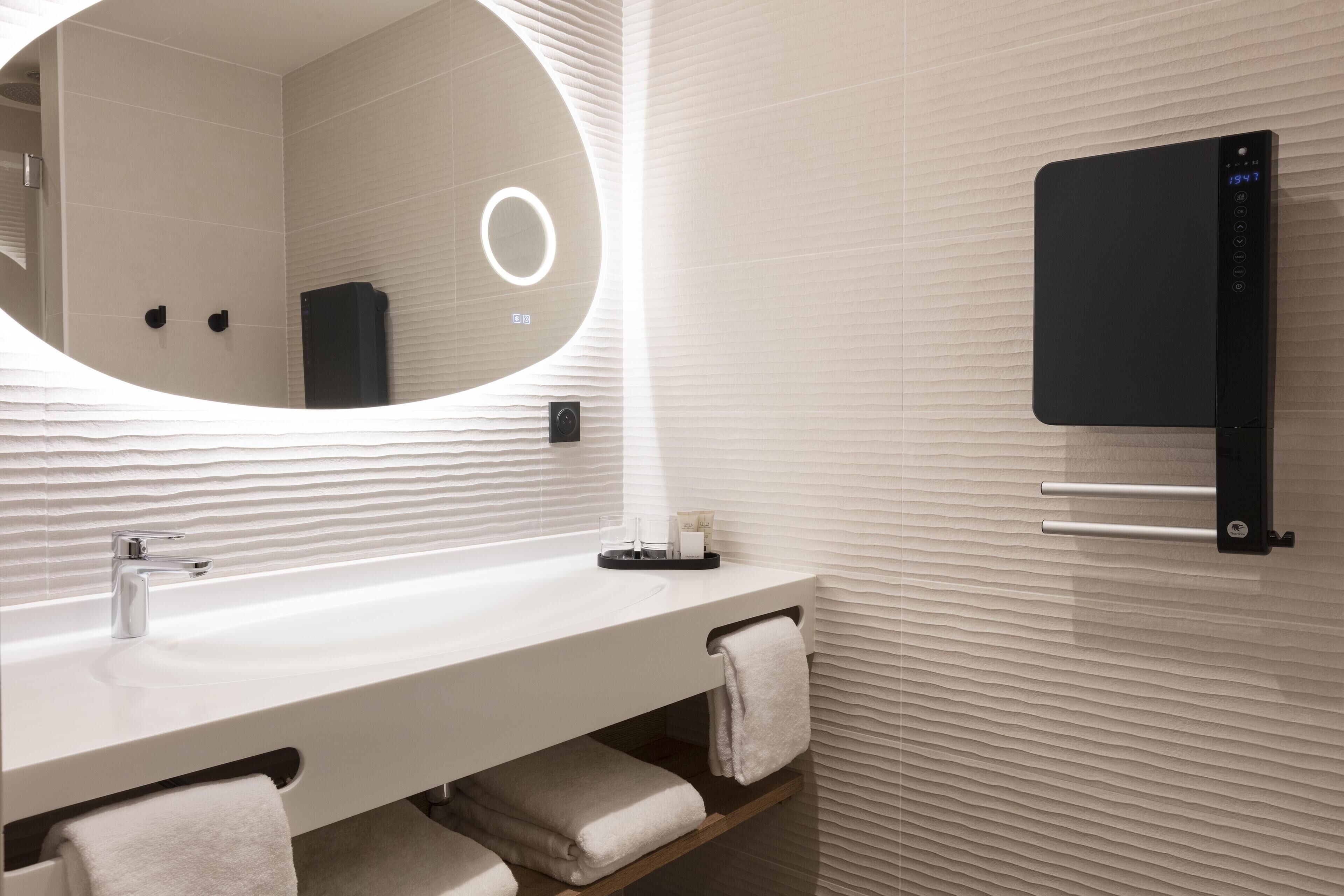 Une salle de bain moderne avec un meuble-lavabo blanc, un grand miroir et un porte-serviettes.